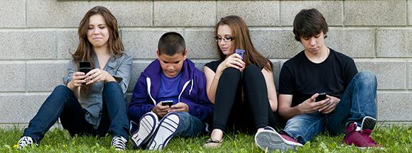 Group of teenage friends sitting outdoors and using cellphone, Model: Brittany Beaudoin, Braden Beaudoin, Cassandra Kosmayer and Ryan Kosmayer